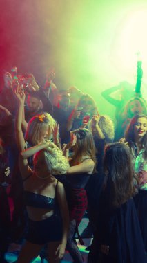 Group of stylish young people dancing with drinks in Halloween themed party. Concept of entertainment, alcohol branding, holiday advertising, youth lifestyle and nightlife.
