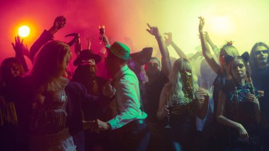 Crowd dancing with colorful lights in Halloween themed nightclub party atmosphere. Concept of entertainment, holiday advertising, youth culture, music industry, emotions, nightlife branding.