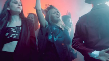 Young women in creative costumes dancing with emotions at club party. Concept of youth culture, fashion advertising, nightlife entertainment, and Halloween celebration.