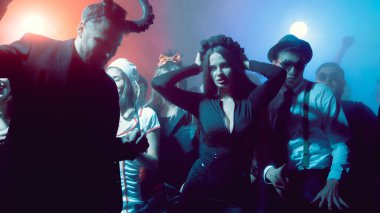 Young woman in black dress dancing at nightclub Halloween party with dramatic lights. Concept of holiday advertising, nightlife, youth emotions, music industry and social lifestyle.