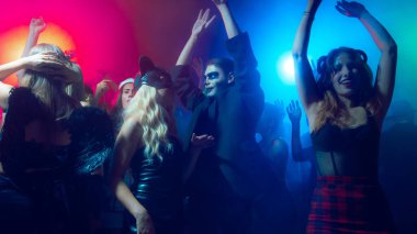 Young woman with horns headpiece dancing on crowded dance floor. Concept of trendy nightlife, music industry, youth Halloween fashion, digital lifestyle and emotional advertising.