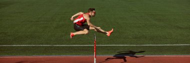 Hurdler jumping over barrier with power and focus during training. Concept of strength, determination, performance for sports marketing, fitness branding, and athlete motivation campaigns. Banner