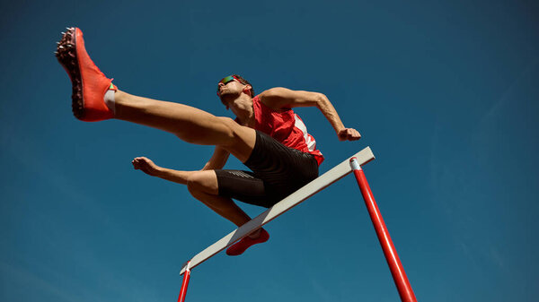 Athlete in red leaping over hurdle with power and confidence under clear sky. Concept of motivation, progress, and strength for sports campaigns, leadership visuals, and athletic branding.