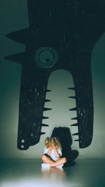 Creative collage. Little girl hiding face under giant monster mouth shadow on green wall. Concept of fear, vulnerability, emotional sensitivity for psychology, therapy and children imagination visuals