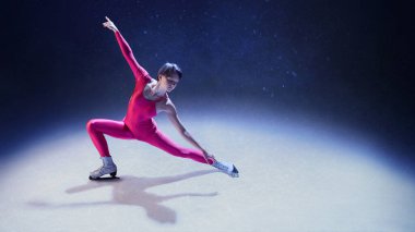 Buz üstünde dinamik duygusal duruş içinde kollarını ve bacaklarını esneten pembe elbiseli kadın artistik patinajcı. İfade gücü kavramı, hareket yoluyla uyum, farkındalık ve hareket halindeki zarafet..