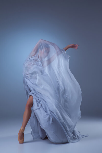 The beautiful ballerina dancing in long blue dress on blue background