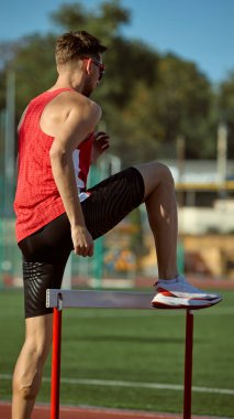 Koşu pistinde ısınma turunda erkek sporcu bacak esnetiyor. Esneklik kavramı, hazırlık, atletik eğitime odaklanma, spor markalaşması ve spor motivasyonu görselleri.