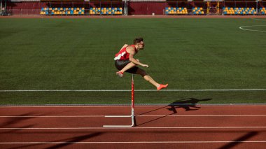 Erkek sporcu atletizm pistinde engeli aşıyor. Hareket kavramı, güç, spor reklamları için kararlılık, atletik markalaşma ve fitness kampanyalarında motivasyon görselleri.