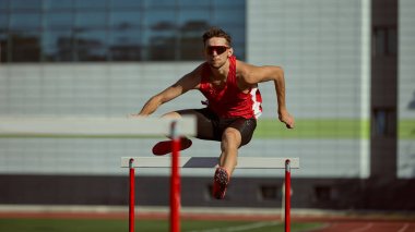 Atletizm atletizm pistte büyük bir kararlılık ve hassasiyetle engelin üzerinden atlıyor. Atletik mükemmeliyet, odaklanma, spor kampanyaları için azim, motivasyon tasarımı ve markalaşma görselleri kavramı.