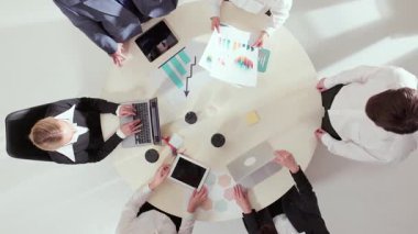 Çeşitli iş adamlarının yuvarlak masa etrafında çizelgeleri ve dizüstü bilgisayarları tartışmalarının en üst görüntüsü. İşbirliği, liderlik, finansal planlama ve analitik duygularla odaklanmış takım çalışması kavramı.