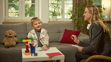 Renkli yaratıcı materyallerle seans sırasında psikologla konuşan gülümseyen çocuk. Pozitif öğrenme, duygusal terapi, farkındalık ve sağlık iletişimi için eğitim psikolojisi kavramı.