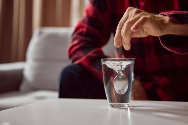 Yaşlı insan ilaç hazırlamak için metal kaşık kullanarak bardağa su karıştırıyor. Eczane eğitimi, klinik eğitim ve önleme içeriği tasarımı kavramı.