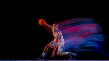 Basketbolcu siyah arka planda top ve neon hareketleriyle çömeldi. Spor eğitimi kavramı, tepki hızı, koçluk tekniği ve modern fitness medyası.