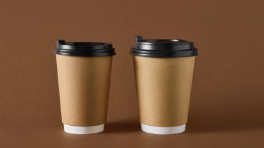 Paket tasarımı için kahverengi arka planda siyah kapaklı iki kahve fincanı. İçecek markası kavramı, sürdürülebilir ambalaj, kafe ve yemek servisi için ürün modeli.