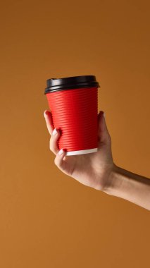 Elinde kırmızı kahve fincanı, portakal arkaplanında siyah kapaklı içecek markası için. Kafe ürün ambalajlama, pazarlama sunumu ve reklam modellemesi kavramı