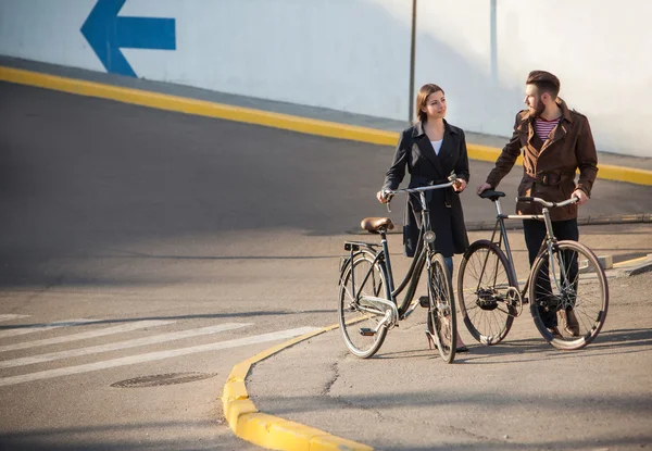 Pareja joven con una bicicleta frente a la ciudad — Foto de Stock