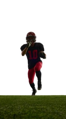Amerikalı futbolcu, yeşil alanda yoğun duygularla ilerlerken beyaz arka planda izole edildi. Güç kavramı, spor reklamı, atlet gelişimi, performans.