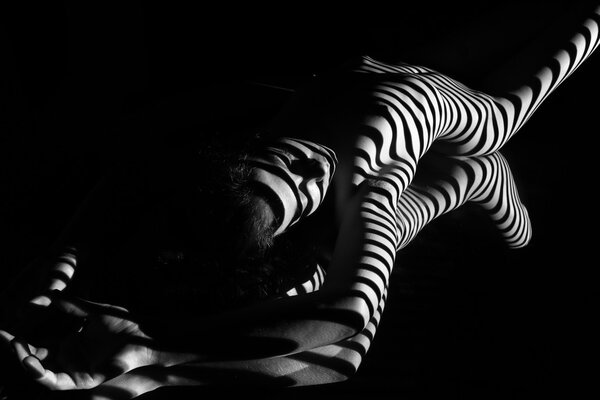 The nude woman and her reflection with black and white zebra stripes. Black-and-white photo created with the projector