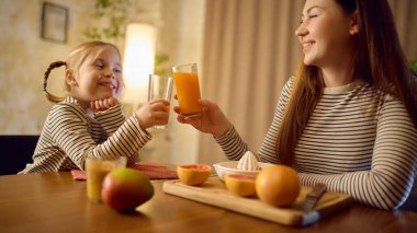 Anne ve kızı sıcak, mutlu bir mutfak sahnesinde taze portakal suyuyla tost yapıyorlar. İçki görselleri, sıcak aile duyguları ve sağlıklı yaşam tarzı tanıtımı kavramı.