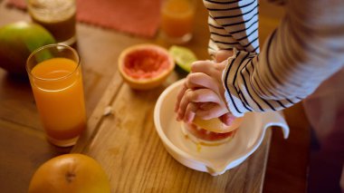 Küçük kız küçük elleriyle narenciye sıkarken taze portakal suyu masada. İçki promosyonu, aile yaşam tarzı görsel ve duygusal sıcak hikaye anlatımı kavramı.