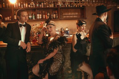 Retro bar sahnesinde çekici kadınlar klasik kıyafetlerle rahatça poz veriyorlar. Moda yaşam tarzı kavramı, lüks markalaşma, gece hayatı kampanyaları, zarif modaya uygun eski hikaye anlatımları..