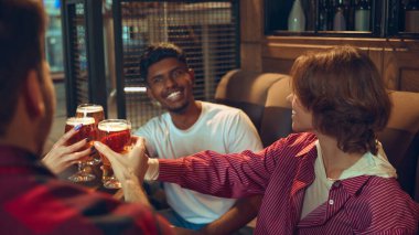 Arkadaşlar bar köşesinde bira bardaklarını alkışlıyorlar. Bira fabrikası hikaye anlatımı, bar reklamcılığı, gece hayatı markalaşması, sosyal eğlence görselleri ve içecek pazarlaması kavramı..