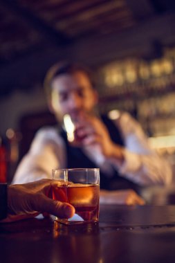 Bar tezgahında el ele tutuşan kehribar içkisi. Bar servisi iş akışı kavramı, günün sonunda gevşeme, içecek siparişi dakikaları ve el yapımı içecek sunumu.