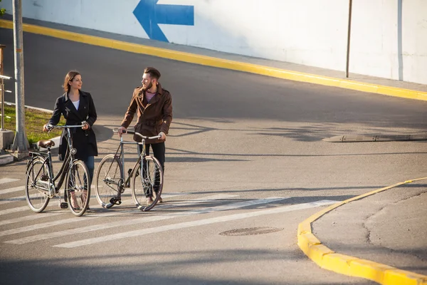 Pareja joven con una bicicleta frente a la ciudad — Foto de Stock
