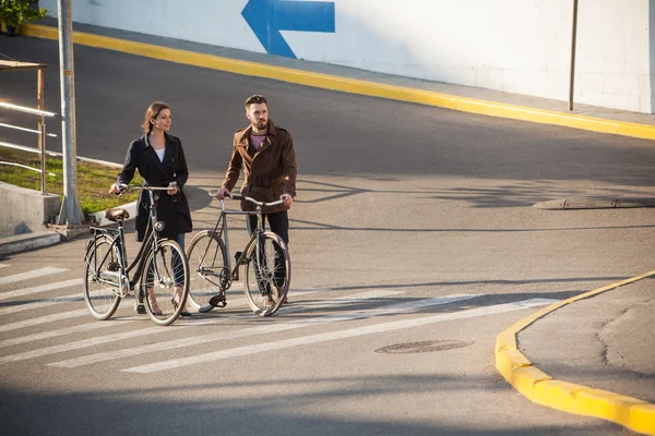 Pareja joven con una bicicleta frente a la ciudad —  Fotos de Stock