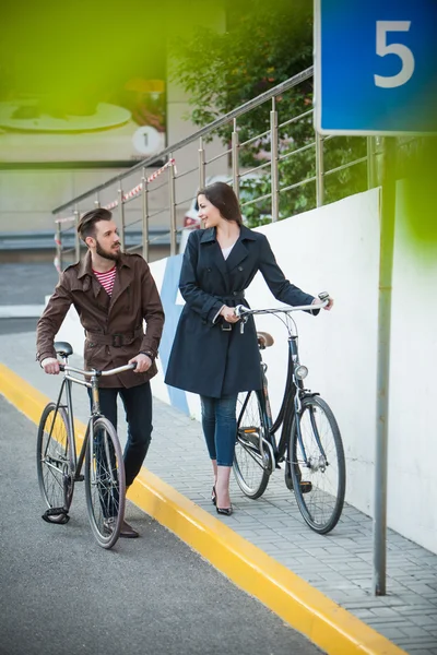 Pareja joven con una bicicleta frente a la ciudad — Foto de Stock