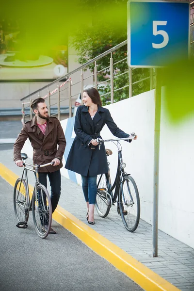 Pareja joven con una bicicleta frente a la ciudad — Foto de Stock