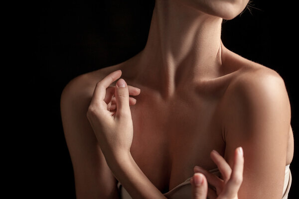 The close-up of a young womans neck and hands on dark background