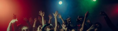 Renkli sahne ışıkları altında ellerini kaldırmış enerjik parti kalabalığı. Yeni yıl kutlaması, gece hayatı özgürlüğü, toplu eğlence ve canlı müzik atmosferi kavramı. Pankart