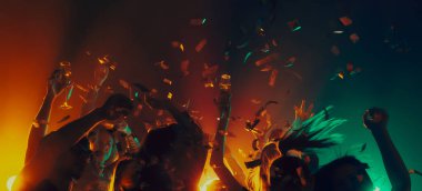 Dramatik kulüp ışıkları altında konfetiyle dans eden kalabalık. Yeni yıl partisinin doruk noktası, geri sayım enerjisi, gece hayatı kaçamağı, müzik güdümlü kutlama ve duygusal rahatlama..