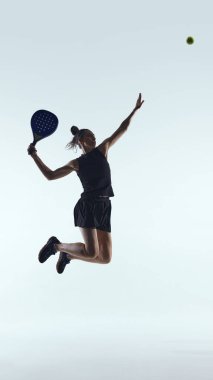 Beyaz arka planda güçlü bir yukarıdan atış için zıplayan dişi Padel oyuncusu. Profesyonel padel sporu, atletik performans, rekabetçi eğitim, modern raket sporu reklamcılığı kavramı.