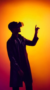 VR kulaklık takan ve parlak turuncu arka plana doğru bakan bir adam. Sanal gerçeklik etkileşimi, teknolojik tanıtım, yenilikçi pazarlama ve gelecekteki kullanıcı deneyimi kavramı.