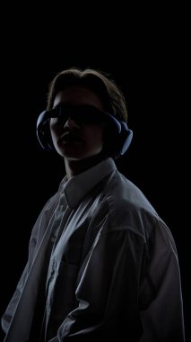 Karanlık stüdyo ışığı altında kulaklık ve güneşlik takan biri. Teknoloji markası kavramı, siber stil başyazıları, elektronik müzik kültürü, moda tanıtımı, gelecekteki kimlik görselleri..