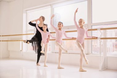 Bale öğretmeni, barda denge egzersizleri sırasında genç dansçılara yardımcı oluyor. Bale öğretmenliği hizmeti tanıtımı, dans eğitimi reklamı, profesyonel koçluk pazarlaması ve stüdyo markalaşması kavramı..