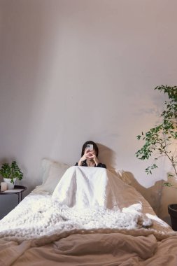 Yatakta tek başına oturan ve akıllı telefon kullanan bir kadın. Kullanıcı hedefleme, kişiselleştirilmiş reklamcılık, mobil abonelik tanıtımı, dijital servis pazarlaması, ev kullanımı bağlamı.