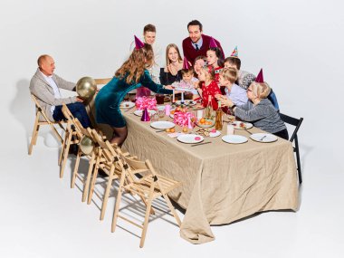 Büyük bir aile doğum gününü pasta ve parti şapkalarıyla kutluyor. Aile odaklı markalar, parti malzemeleri promosyonu, yemek dağıtımı, yaşam tarzı reklamcılığı ve çok nesilli kutlamalar kavramı.