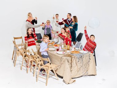 Neşeli çoklu nesil aile Noel yemeğini şenlik masasında kutluyor. Bayram yemekleri reklamı, aile yaşam tarzı markalaşma, içecek promosyonu ve mevsimlik kampanyalar kavramı.