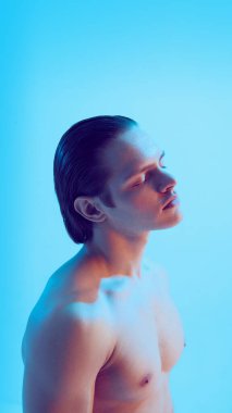 Mavi stüdyoda duygusal bakışları olan genç bir adam portresi. Kırılganlık kavramı, kişisel yansıma, duygusal derinlik, modern erkek kimliği ve minimalist estetik..