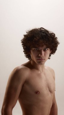 Tarafsız arka planda yoğun bakışlı genç adam portresi. Erkek bakımı, cilt sağlığı, kendine güven markalaşması, editoryal cilt bakımı ve modern erkeklik kavramı..