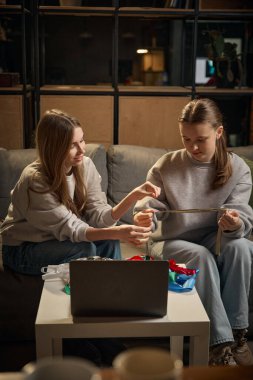 Kız kardeşler evdeki el yapımı proje için dekoratif kurdele ölçüyorlar. Yaratıcı takım çalışması kavramı, diy ustalığı, dikkatli hazırlık, ortak hobi, rahat ev ortamı.