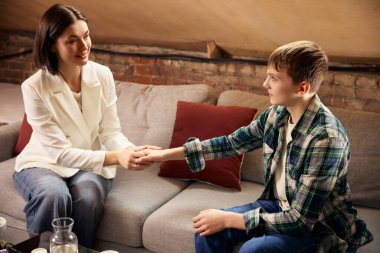 Terapi seansı sırasında genç bir çocuk kadın psikologla el ele tutuşuyor. Duygusal destek, ruhsal sağlık, gençlik danışmanlığı, psikolojik güvenlik ve profesyonel yardım kavramı.