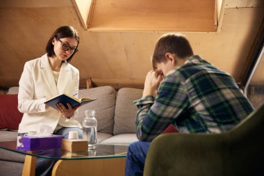 Psikoloji terapisi sırasında ergen çocuk duygusal davranırken uzman not alıyor. Ruh sağlığı desteği, stres yönetimi, profesyonel danışmanlık ve ergen refahı kavramı.