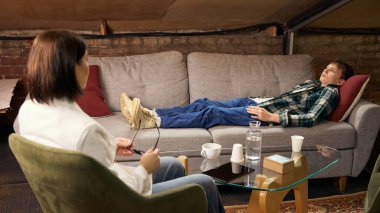 Psikolojik terapi sırasında kanepede yatan bir genç. Profesyonel ruh sağlığı hizmetleri, gençlik psikoterapisi, stres yönetimi, sağlık hizmetleri ve danışmanlık desteği kavramı.