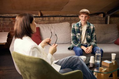 Genç çocuk psikologla psikoterapi seansı sırasında konuşuyor. Ruh sağlığı desteği kavramı, profesyonel danışmanlık hizmetleri, sağlık reklamları görselleri ve özel terapi seansları.