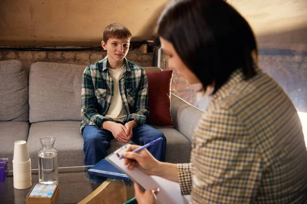 Terapi seansı sırasında psikologla konuşan bir ergen. Ergen akıl sağlığı kavramı, duygusal destek, güven, danışmanlık süreci, güvenli terapi ortamı.