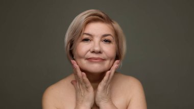Olgun bir kadın yüz derisine dokunuyor. Yaşlanmayı önlüyor. Yüz bakımı tanıtımı, cilt bakımı markalaşması güzellik kampanyası, 50 yaşın üzerindeki kadınlar için kozmetik reklamcılık..
